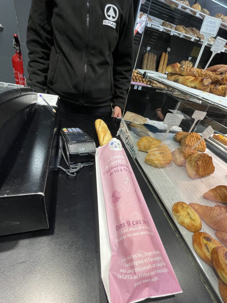 Un sac à pain Octobre Rose et sa baguette au comptoir d'une boulangerie du territoire
