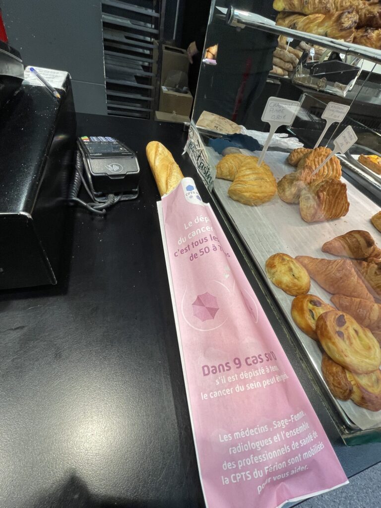 Sac à pain Octobre Rose devant la vitrine de viennoiseries d'une boulangerie partenaire